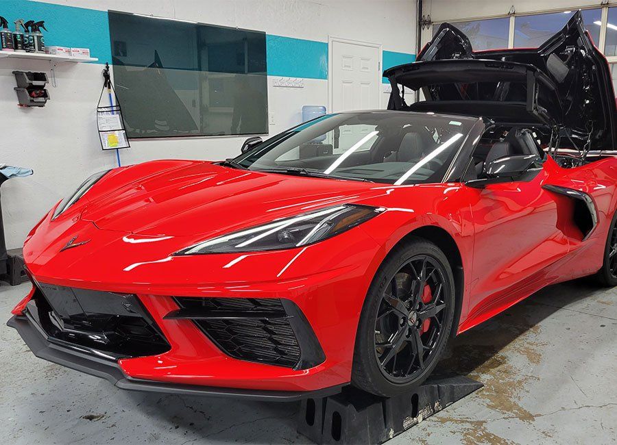 Red Corvette convertible with black wheels and doors open, parked indoors.