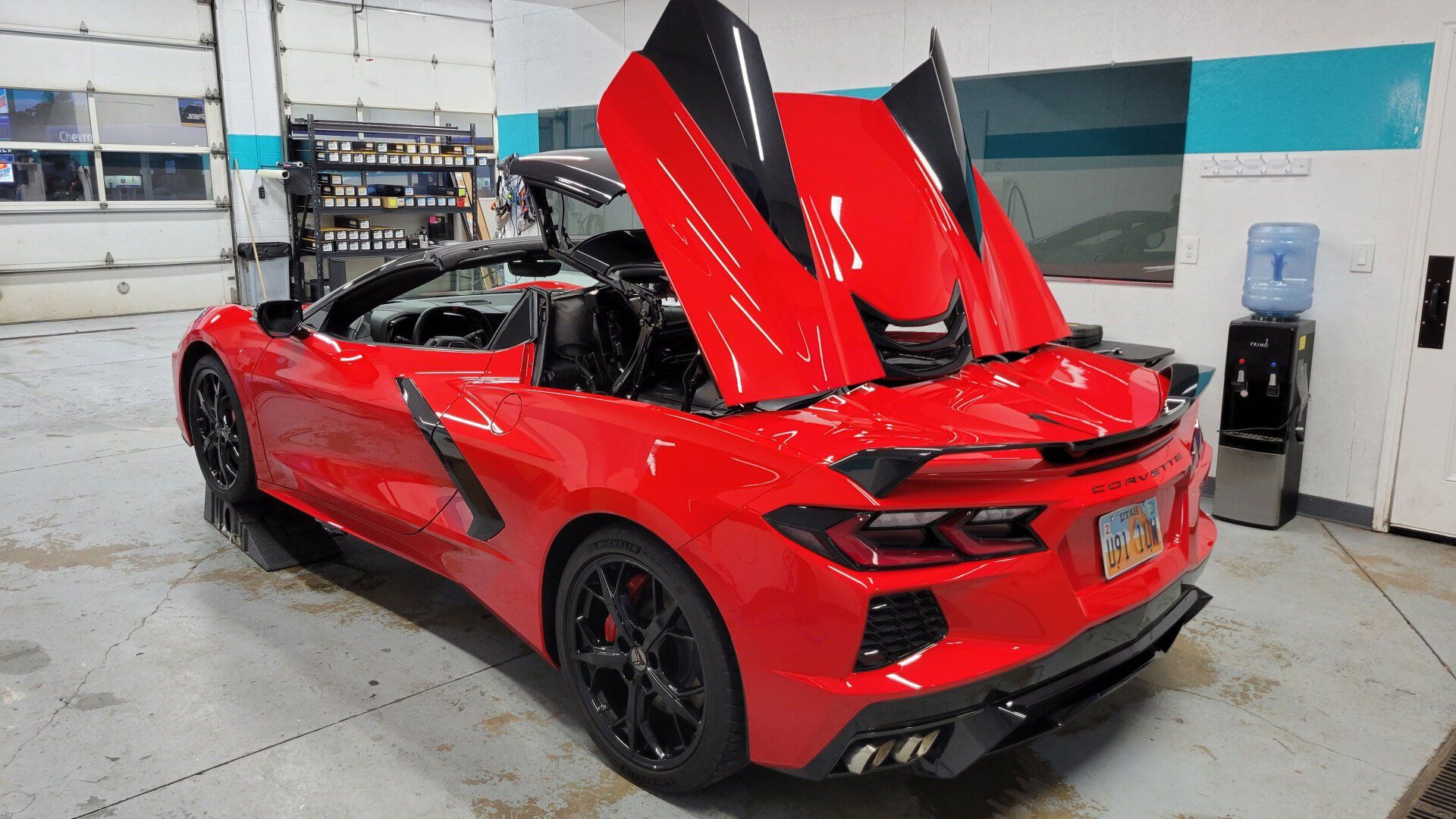 Red convertible sports car with black accents, doors open upwards, inside garage.