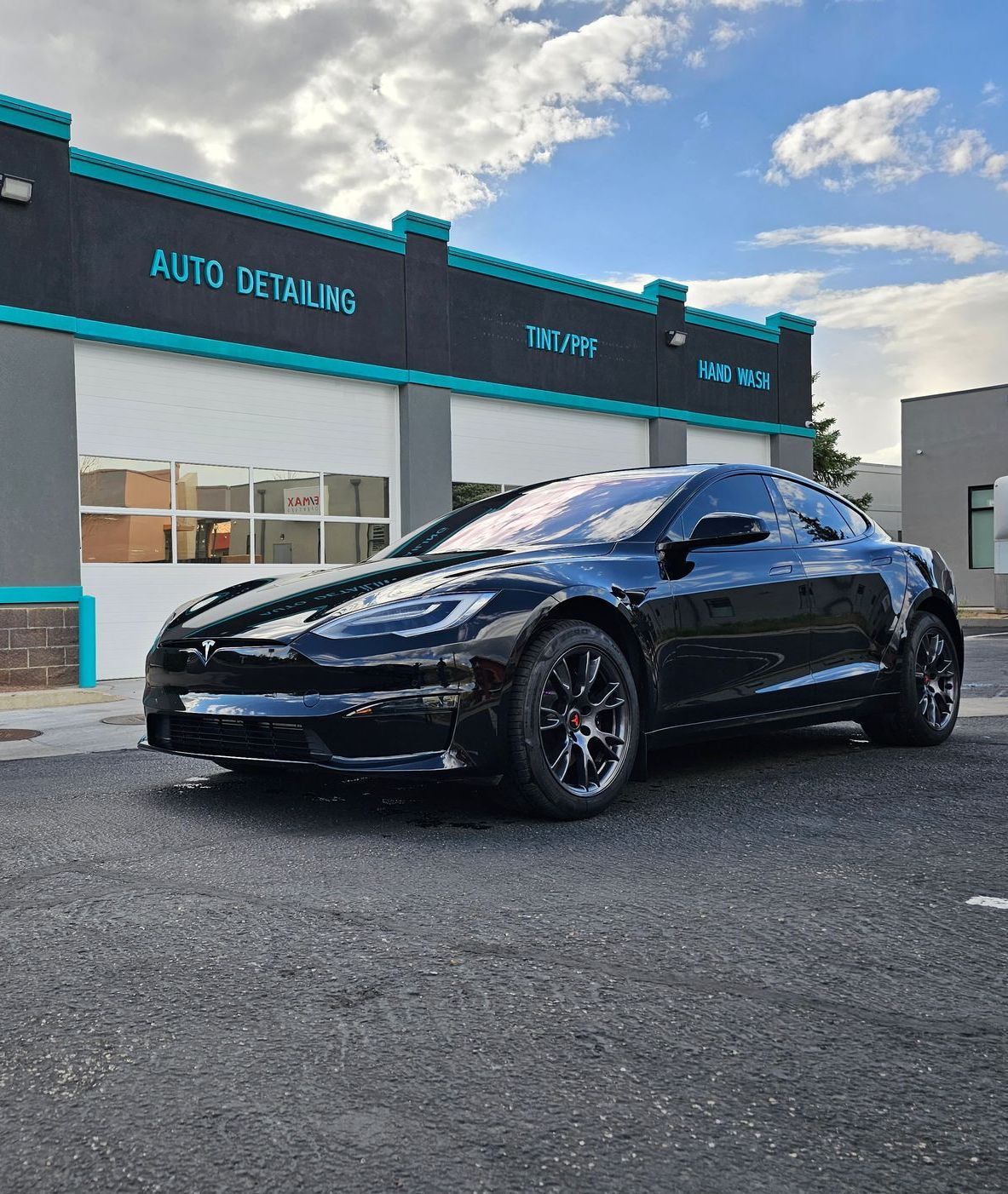 Black Tesla parked in front of an auto detailing business with turquoise trim.