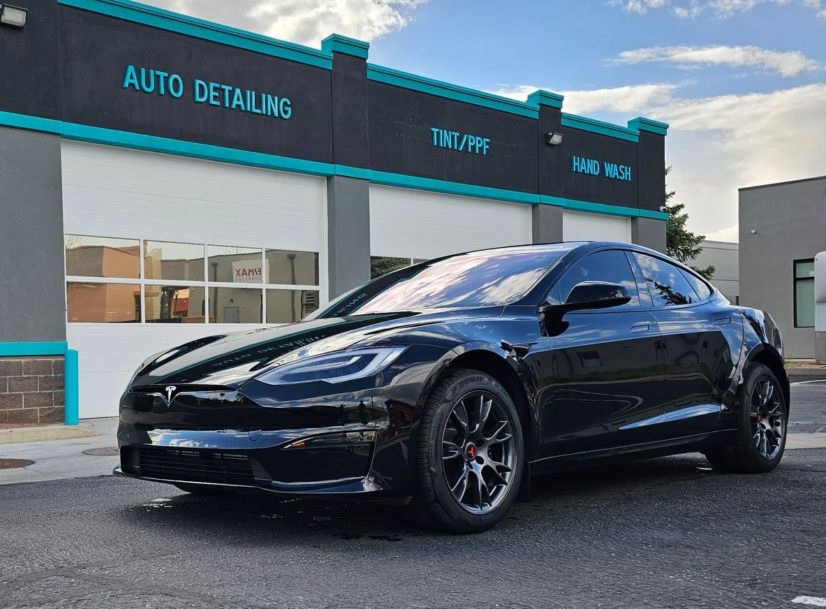 Black sports car parked outside an auto detailing shop under a blue sky
