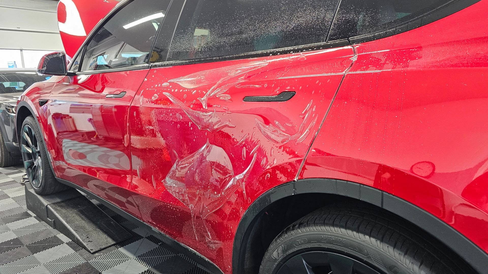 Red Tesla with clear protective film applied to the side panels.