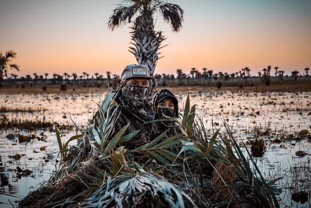 A man in a camouflage suit is sitting in the middle of a swamp.