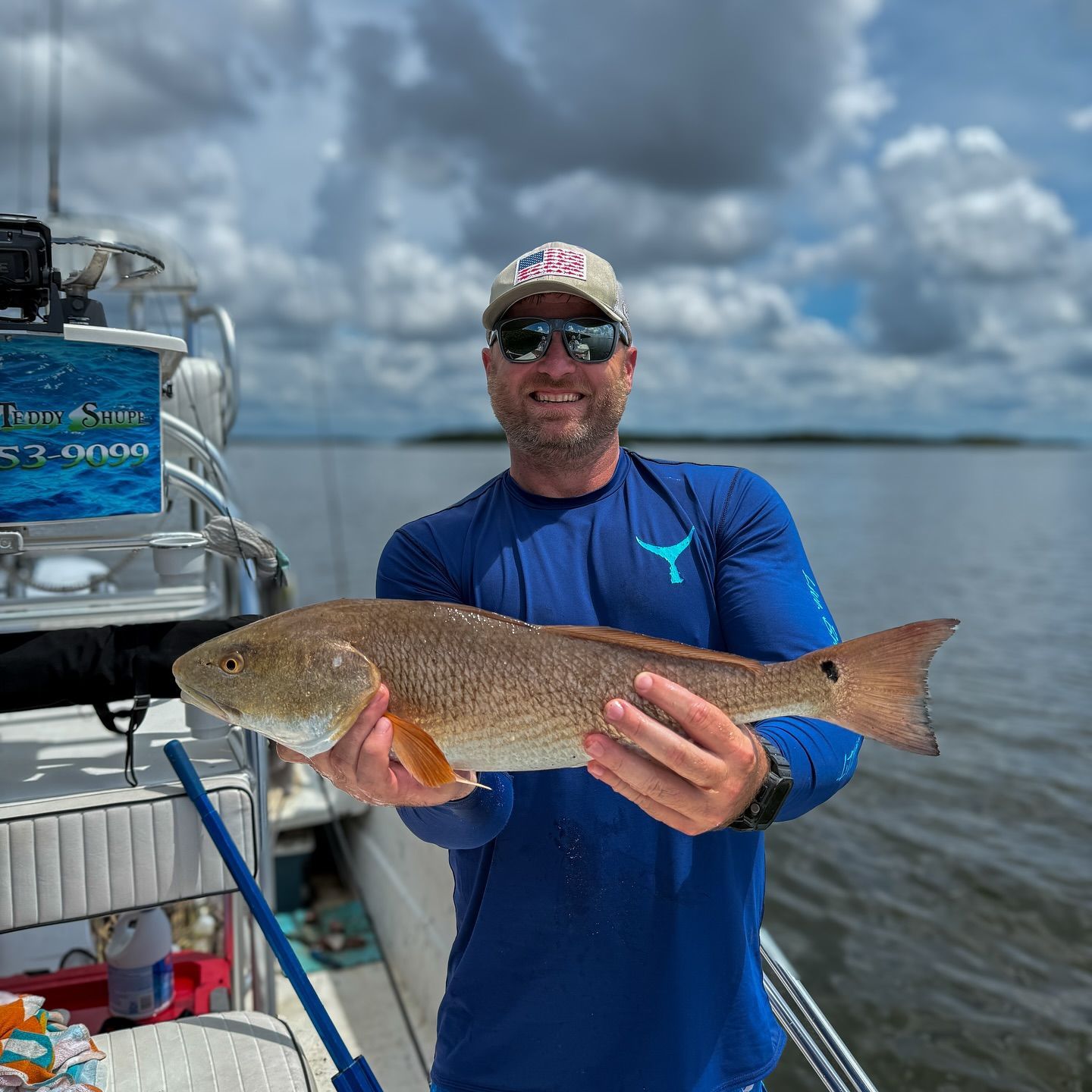 Man holding large redfish on a boat in a coastal setting, smiling.