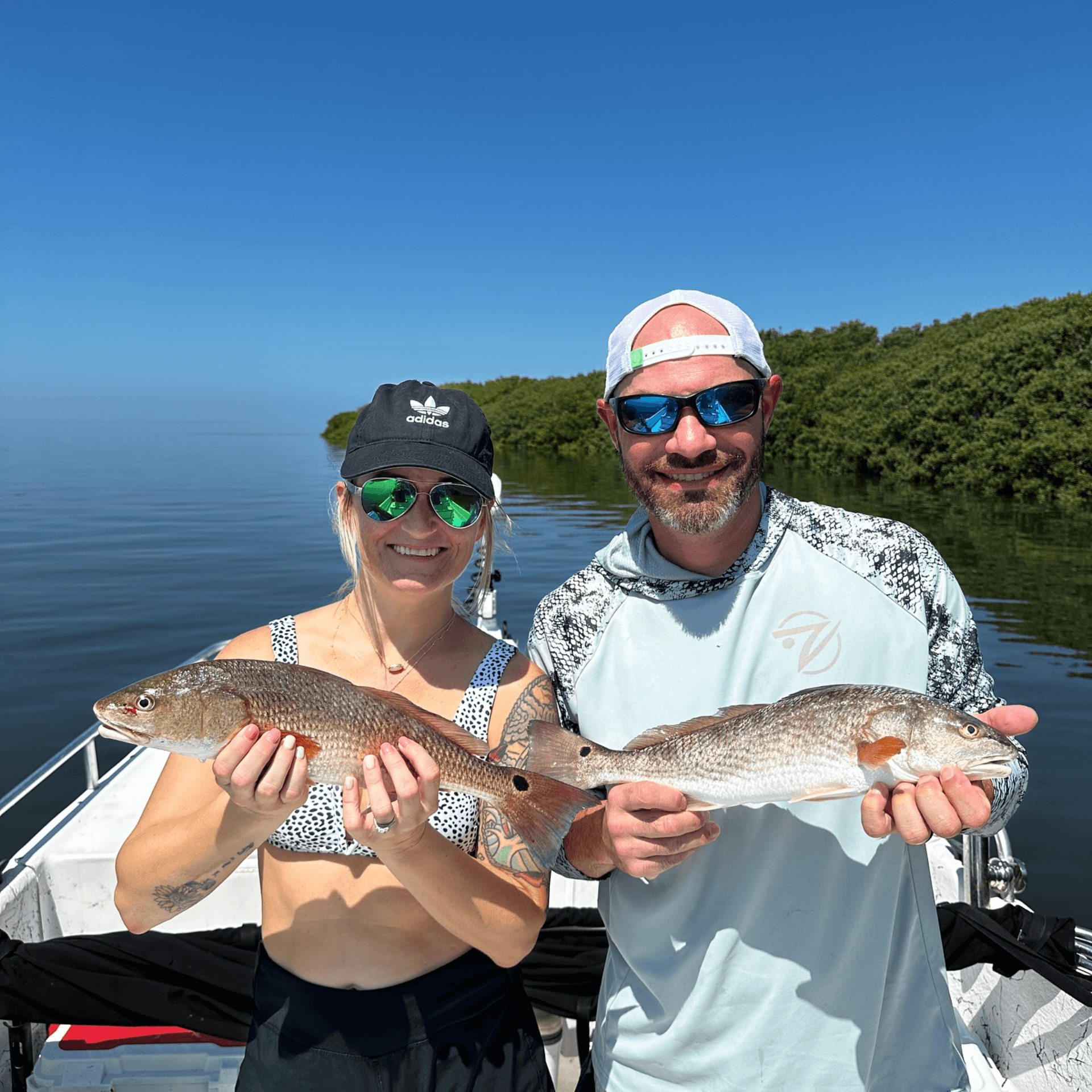 A man and a woman are holding two fish on a boat.