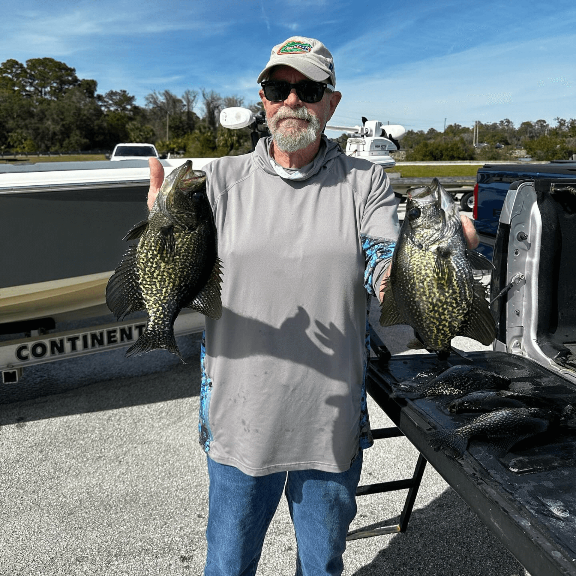 A man is holding two Crappie in front of a truck that says continent