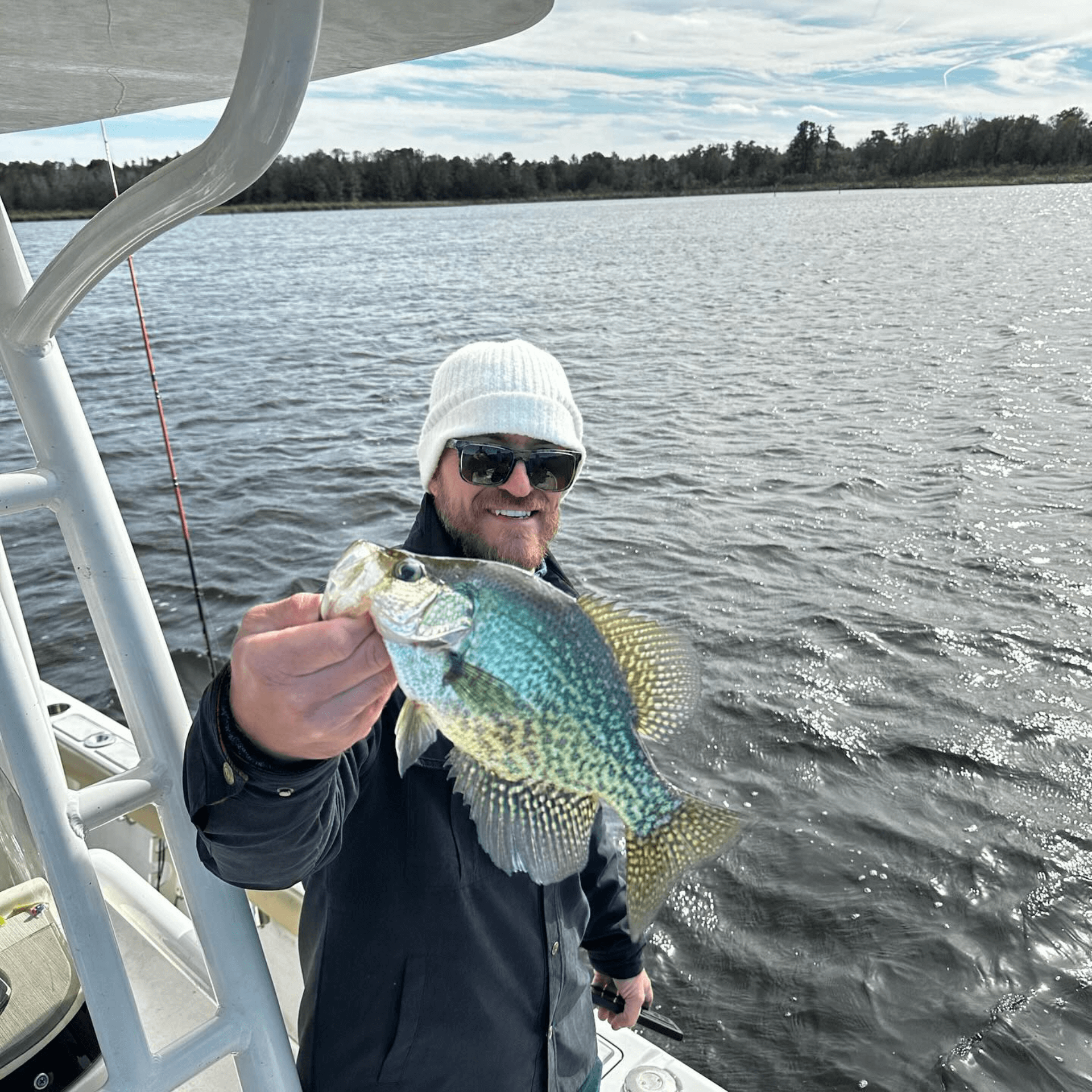 A man is holding a Crappie on a boat in the water.