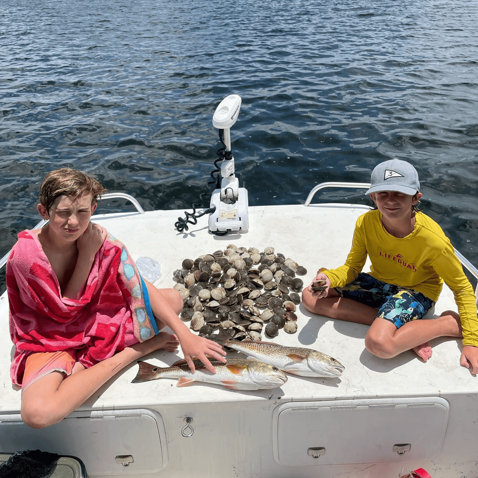 Two children are sitting on the back of a boat holding fish.