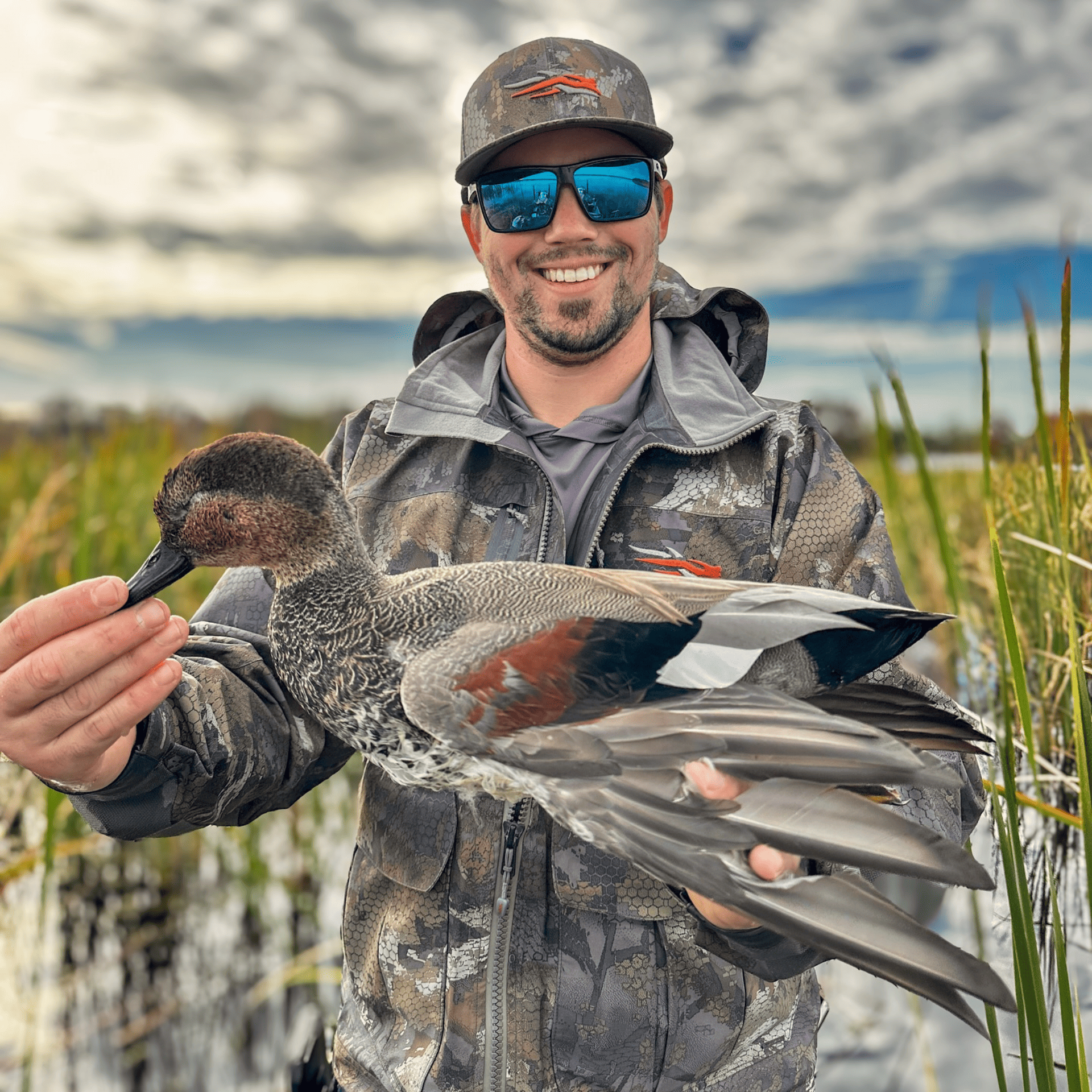 A man is holding a duck in his hands in a field.