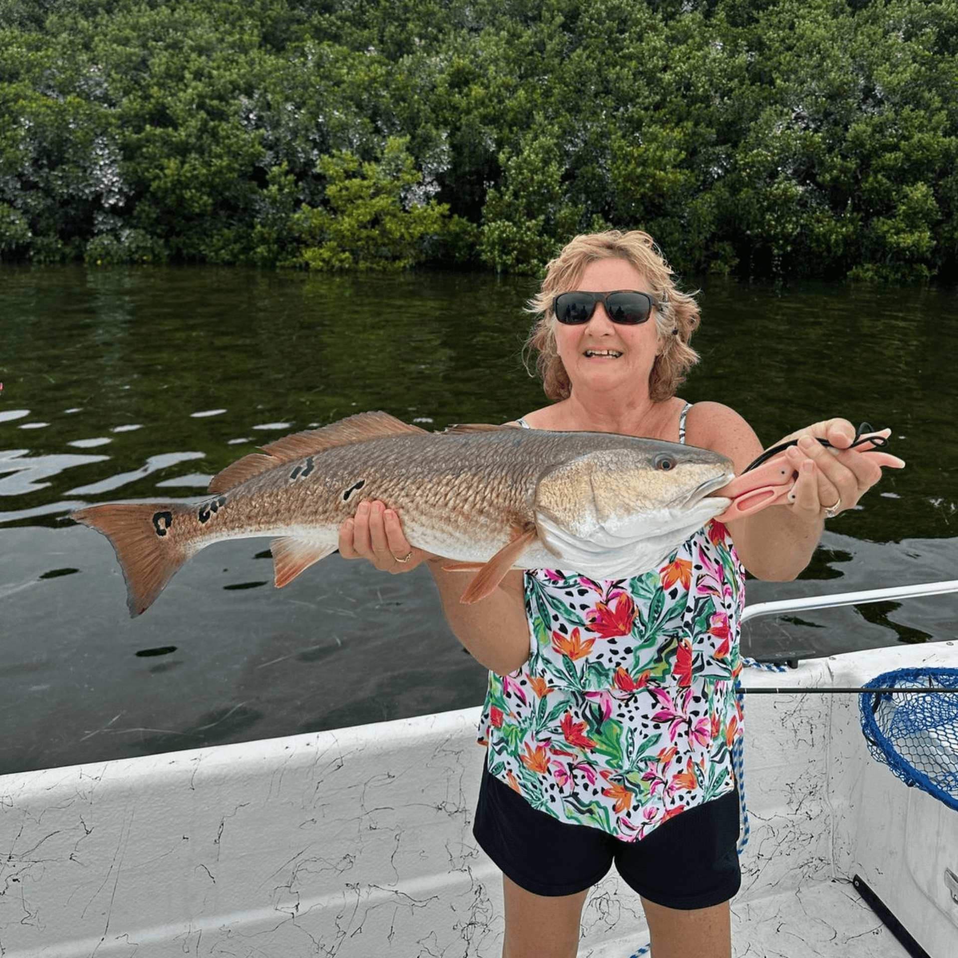 A woman is holding a large Redfish in her hands on a boat.