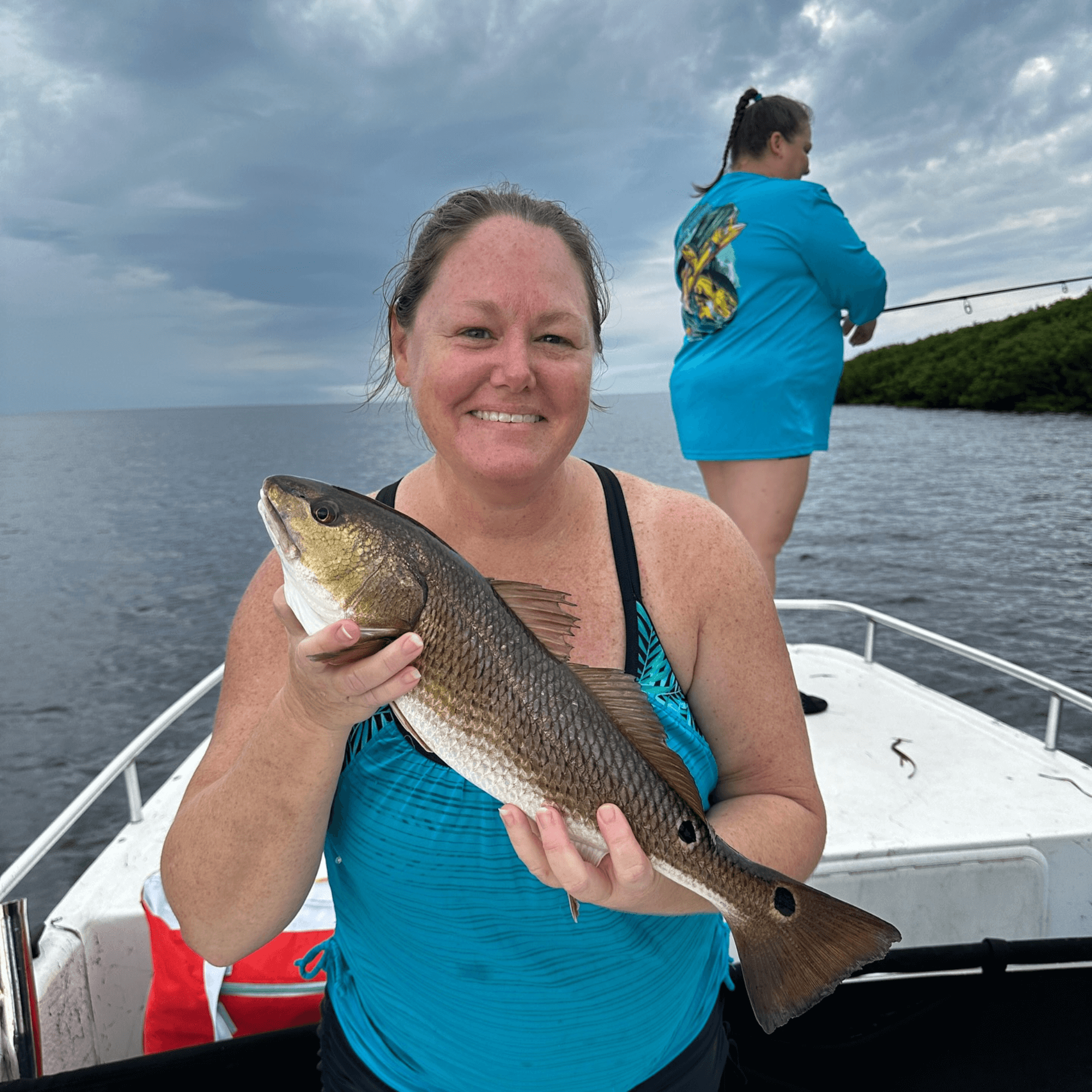 A woman is holding a large fish on a boat