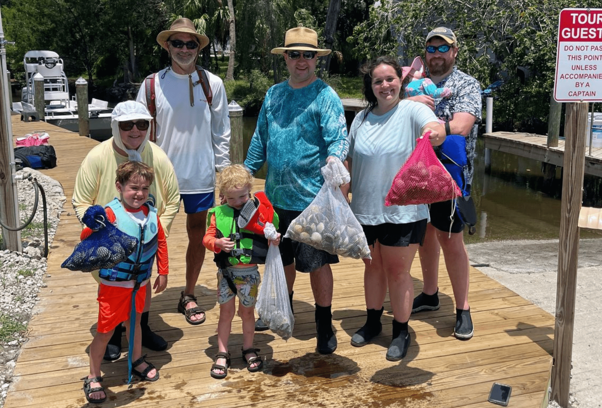 A group of people are standing on a wooden dock holding bags of shells.