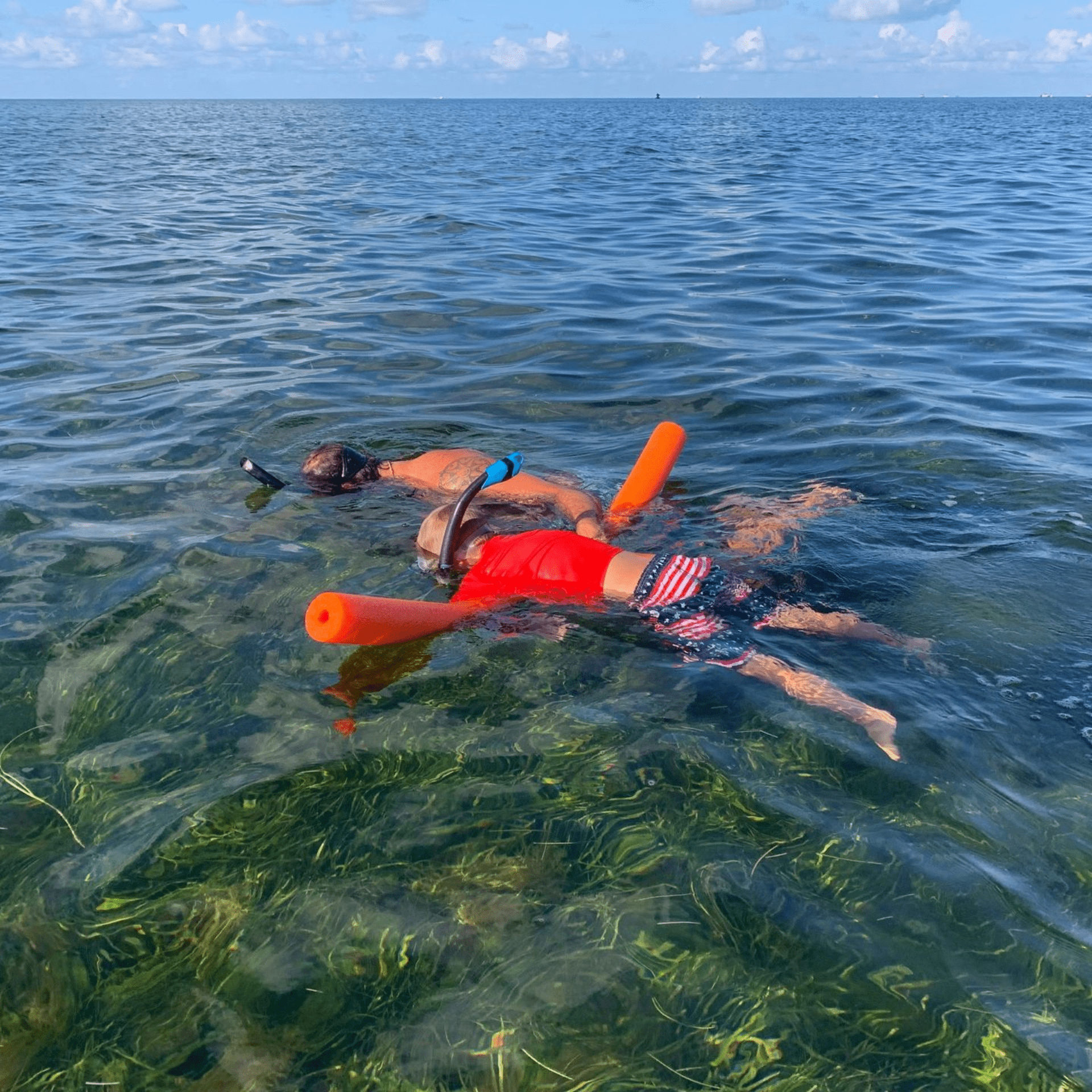 Two people are swimming in the ocean with floats.