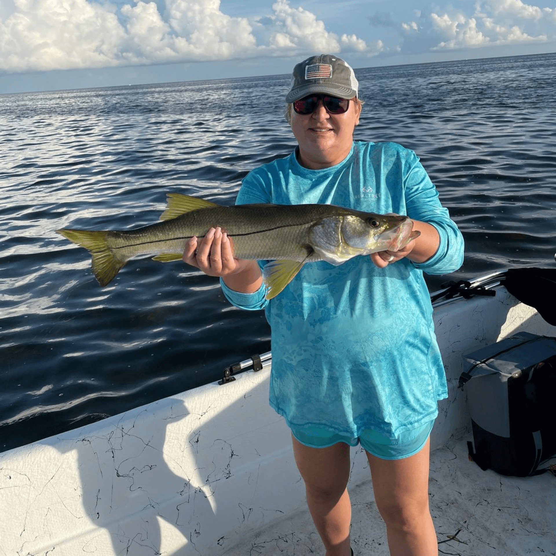 A woman is standing on a boat holding a Snook.