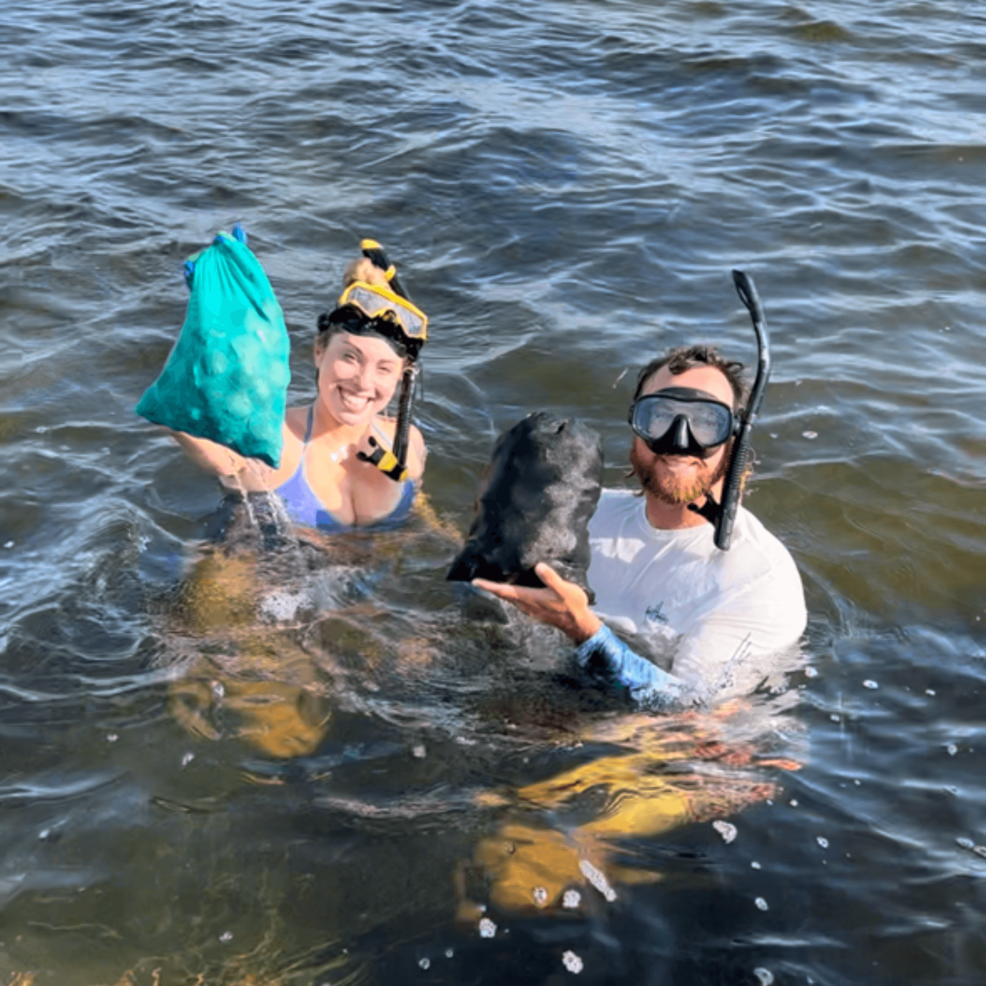 A man and a woman are swimming in the Gulf with bags of scallops