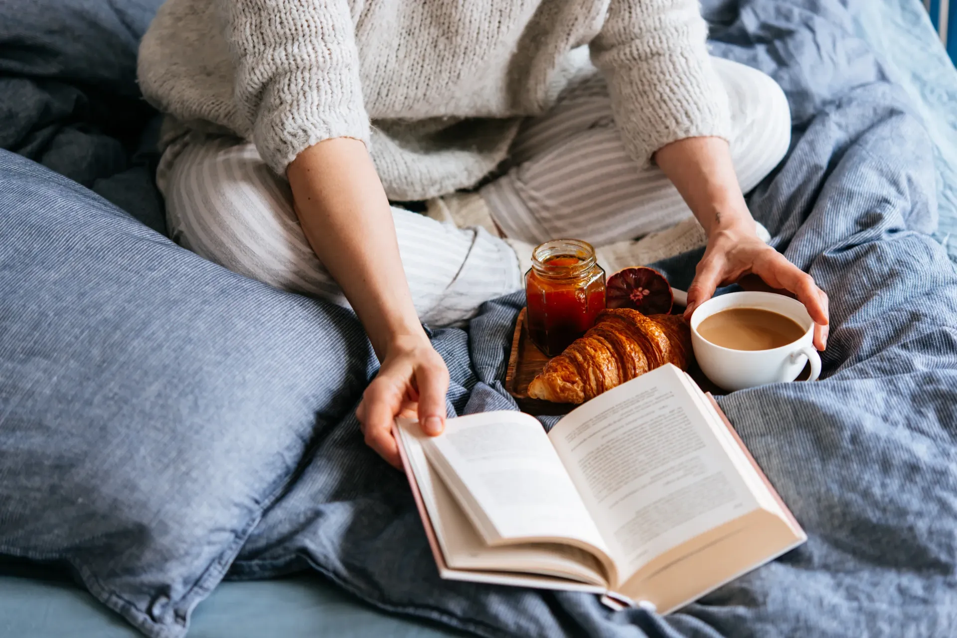 A person enjoying a leisurely breakfast in bed with a book and coffee.