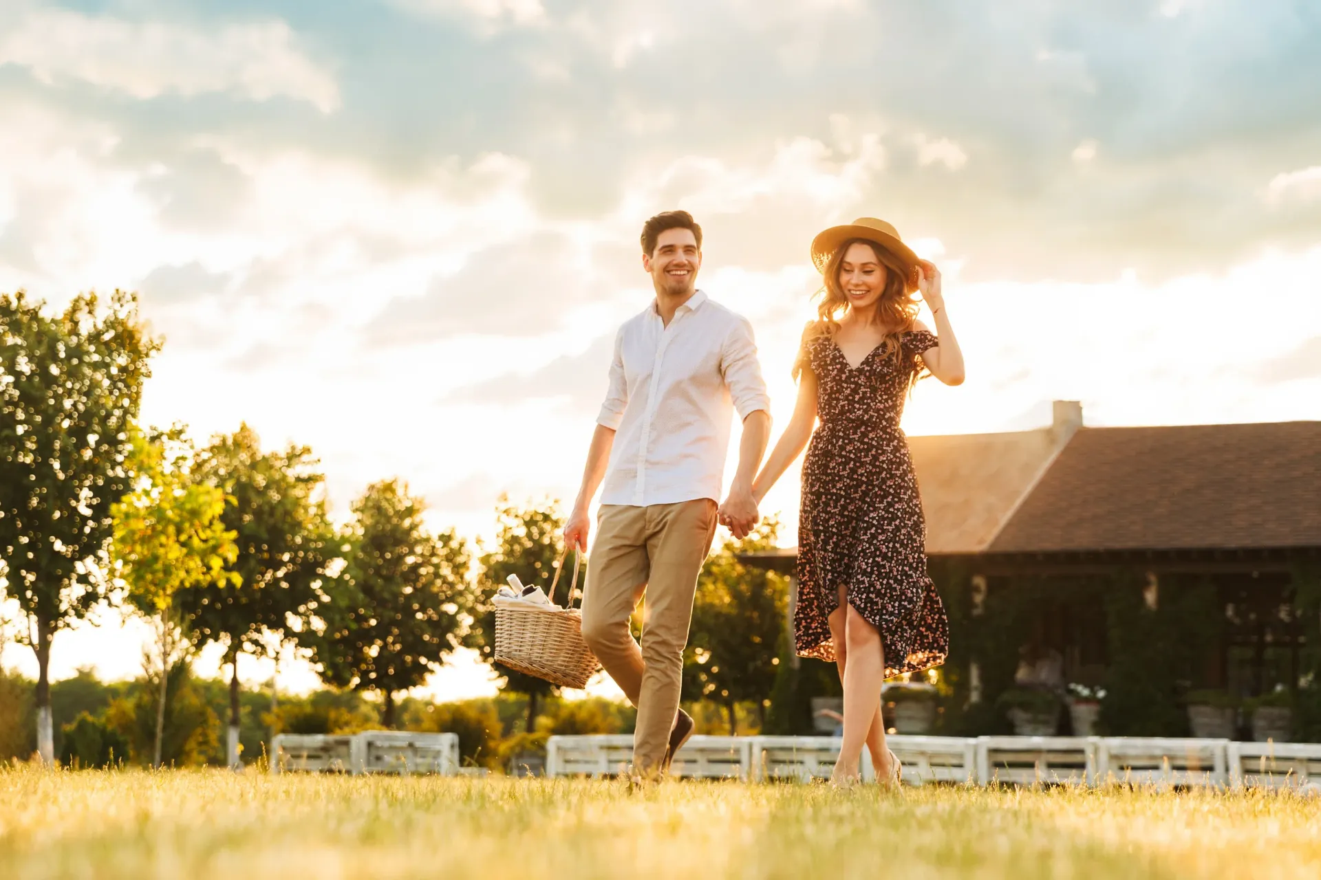 Couple holding hands and walking with a picnic basket during sunset.