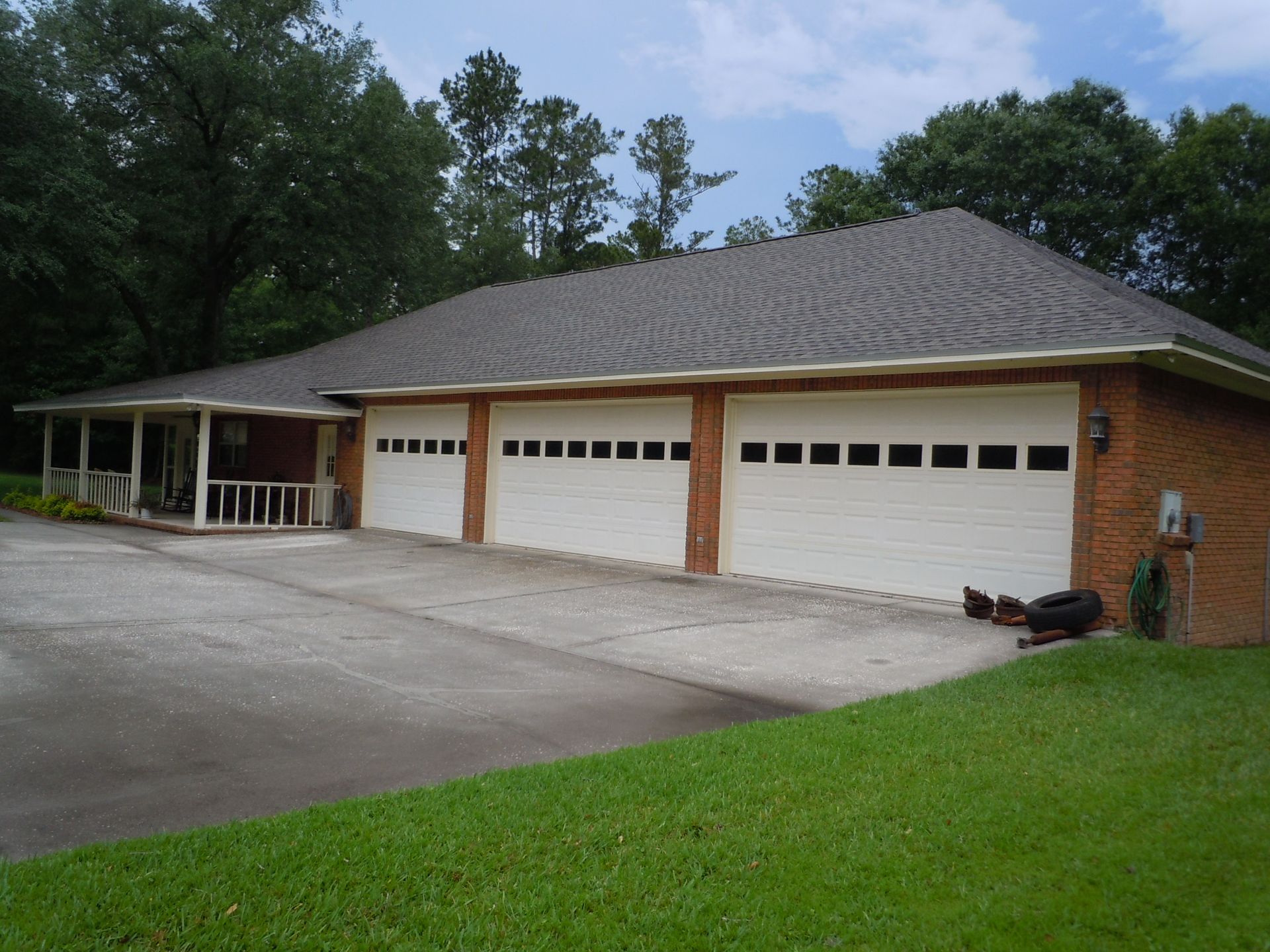 Brick house with four white garage doors, a driveway, and green lawn under trees.