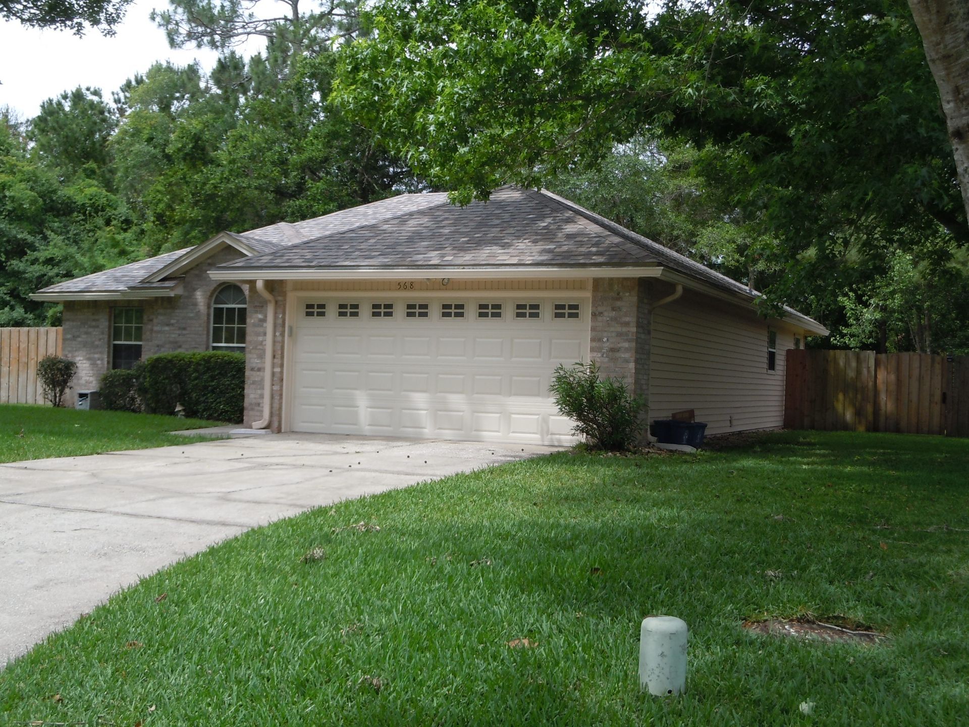 Suburban house with a two-car garage, driveway, and green front lawn under trees.