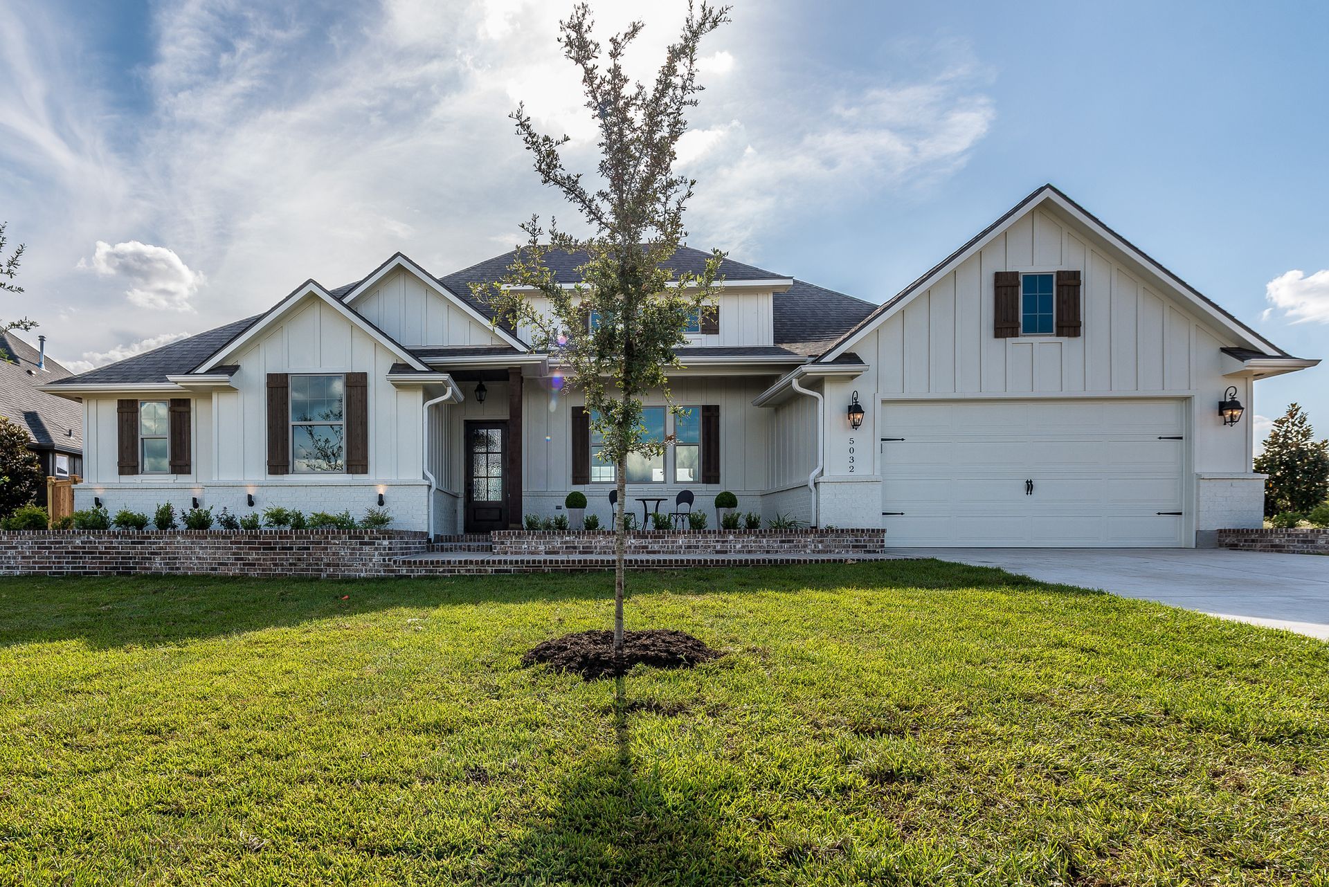 Single-story suburban house with a two-car garage and a young tree in the front lawn