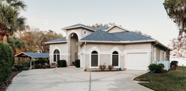 Large stucco house with a blue roof, arched windows, and a wide driveway in a suburban neighborhood