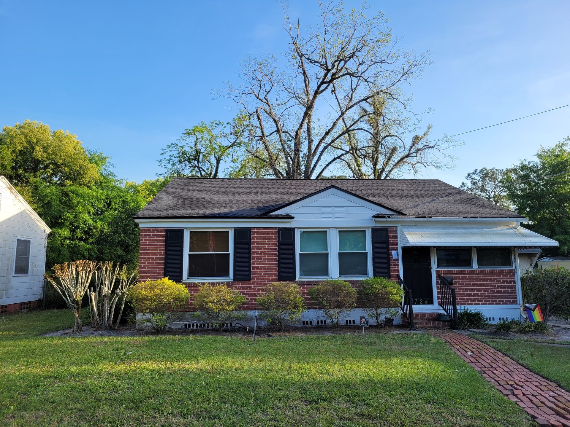 Single-story brick house with white trim, front lawn, and red brick walkway under a clear sky