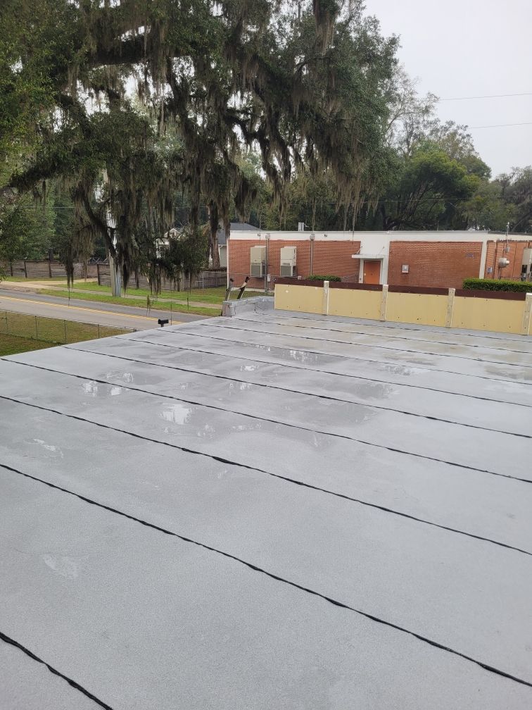 Rainy rooftop with gray metal panels, a large tree, and a brick building in the background