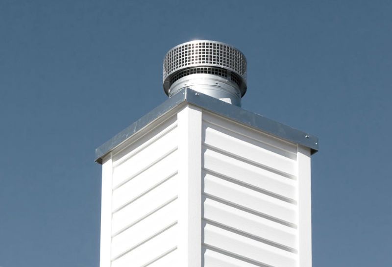 White rooftop vent chimney with a silver cap against a clear blue sky