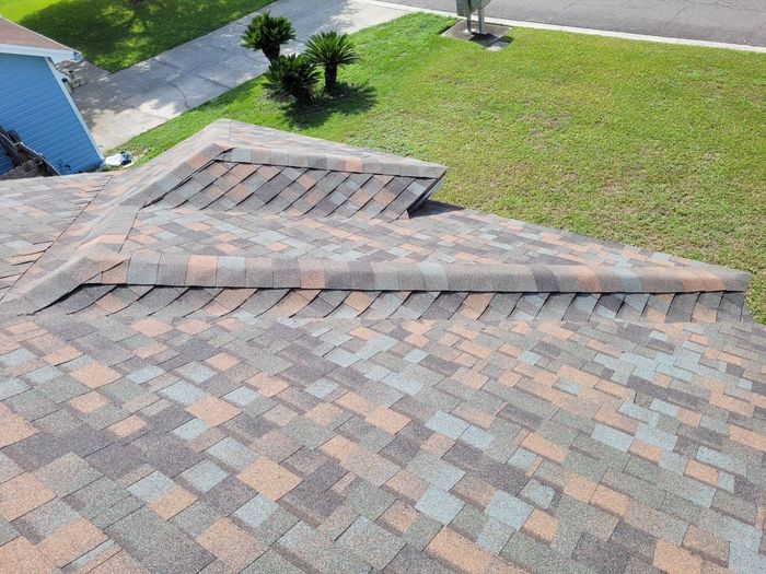 Damaged shingled roof with a large ridge and raised section near a grassy yard