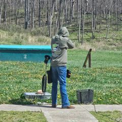Person aiming a rifle at an outdoor shooting range with target and gear nearby