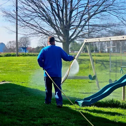 Person watering grass near a playground swing and slide on a sunny day