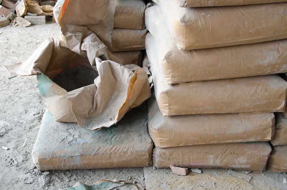 Bags of Cement Stacked on A Rough Surface, One Bag Is Torn Open — Cessnock Landscaping Supplies In North Rothbury, NSW