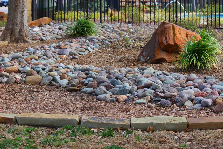 Rock Garden with River of Stones, Trees, and A Large Orange Boulder — Cessnock Landscaping Supplies In Cessnock, NSW