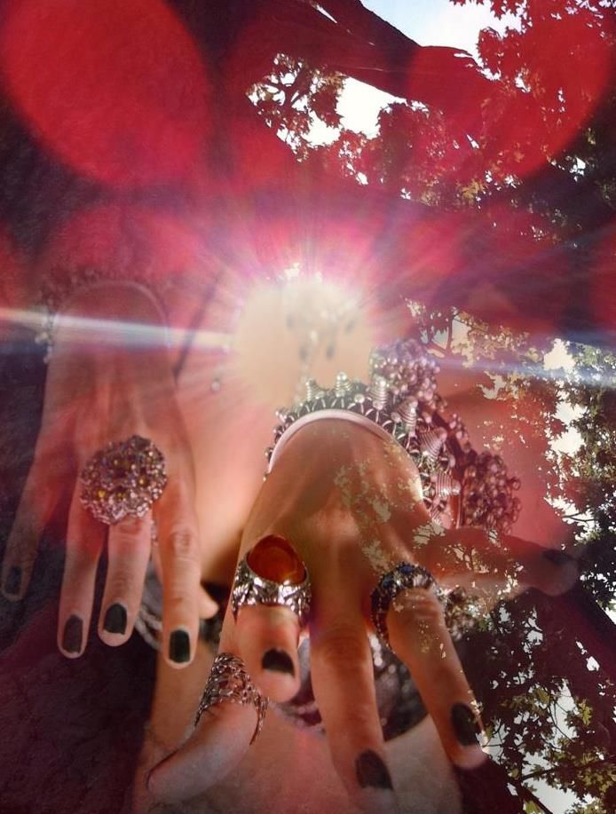 Hands with glittering rings reach toward a bright red sunburst with sparkles.