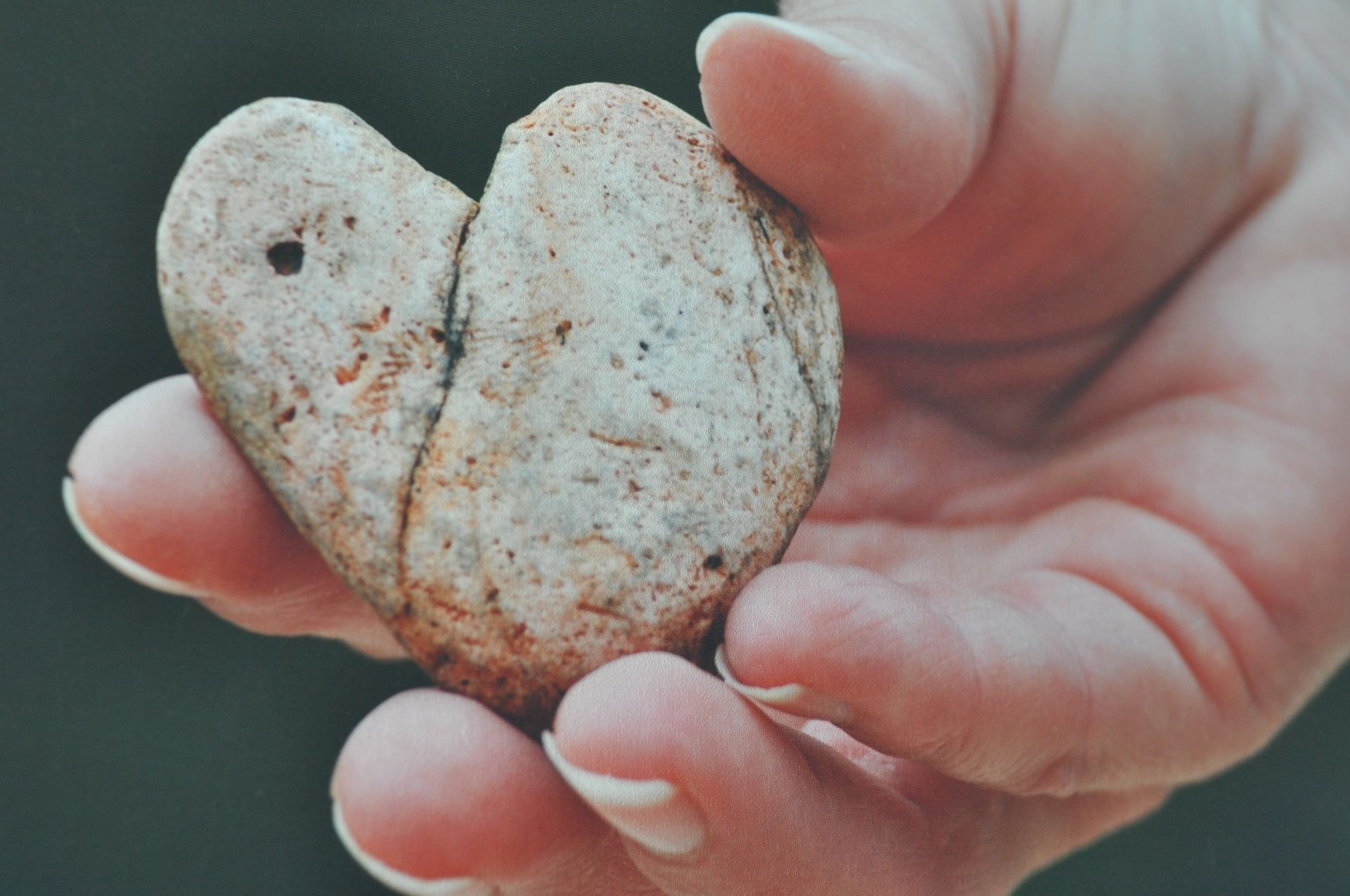 Hands holding a heart-shaped stone outdoors