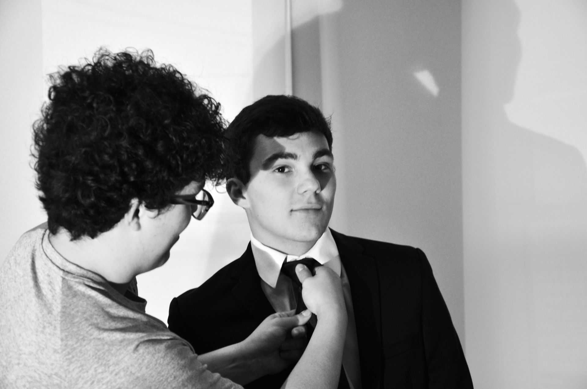 Person adjusting another person’s tie in a black-and-white portrait.