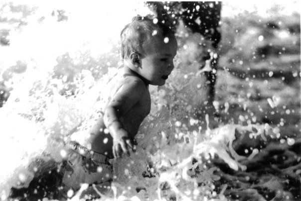 Child splashing in water, surrounded by spray and waves in a bright outdoor scene