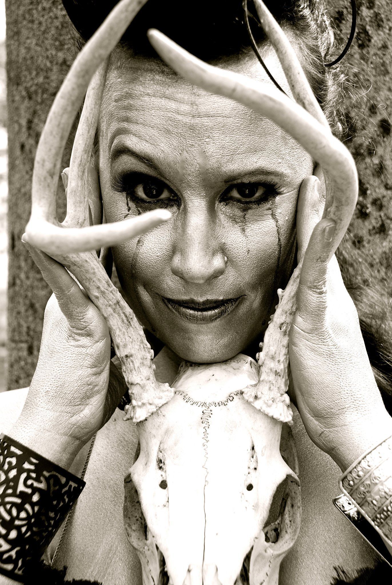 Person framed by large antlers in a sepia-toned portrait, staring directly at the camera.