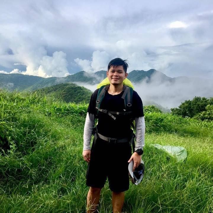 A man with a backpack is standing in a field with mountains in the background.