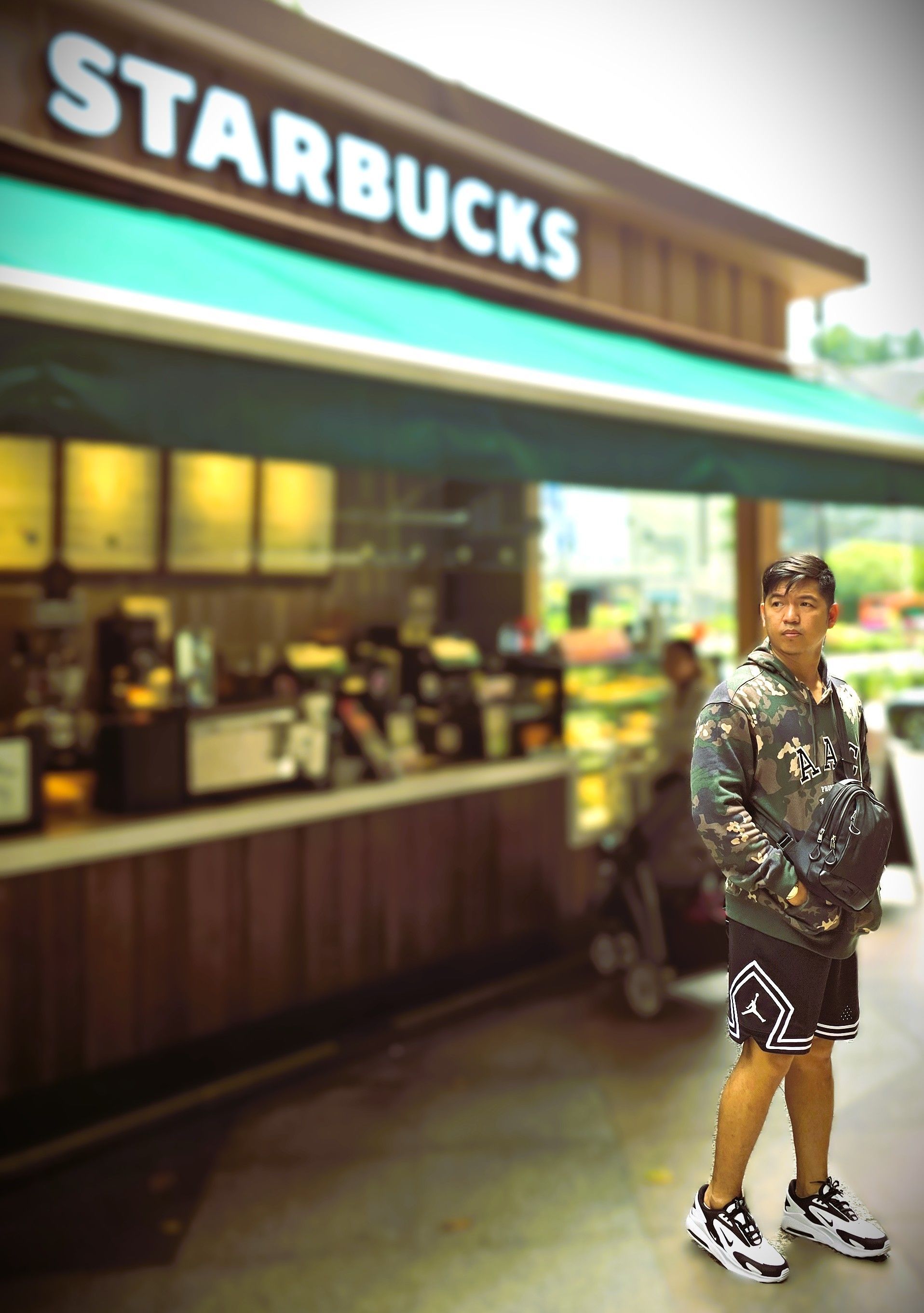 Person standing outside a Starbucks coffee shop at night, with a lit storefront and teal awning.