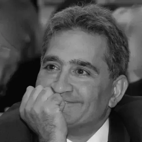 A man in a suit and tie is smiling with his hand on his chin.