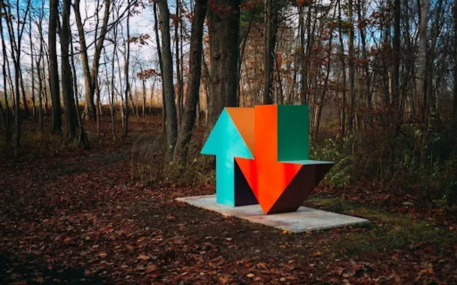 A colorful sculpture of two arrows pointing in opposite directions in the middle of a forest.