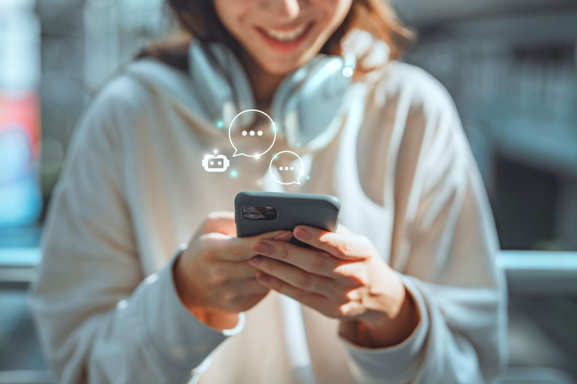 Person in a white hoodie smiling at a smartphone with chat bubbles above it
