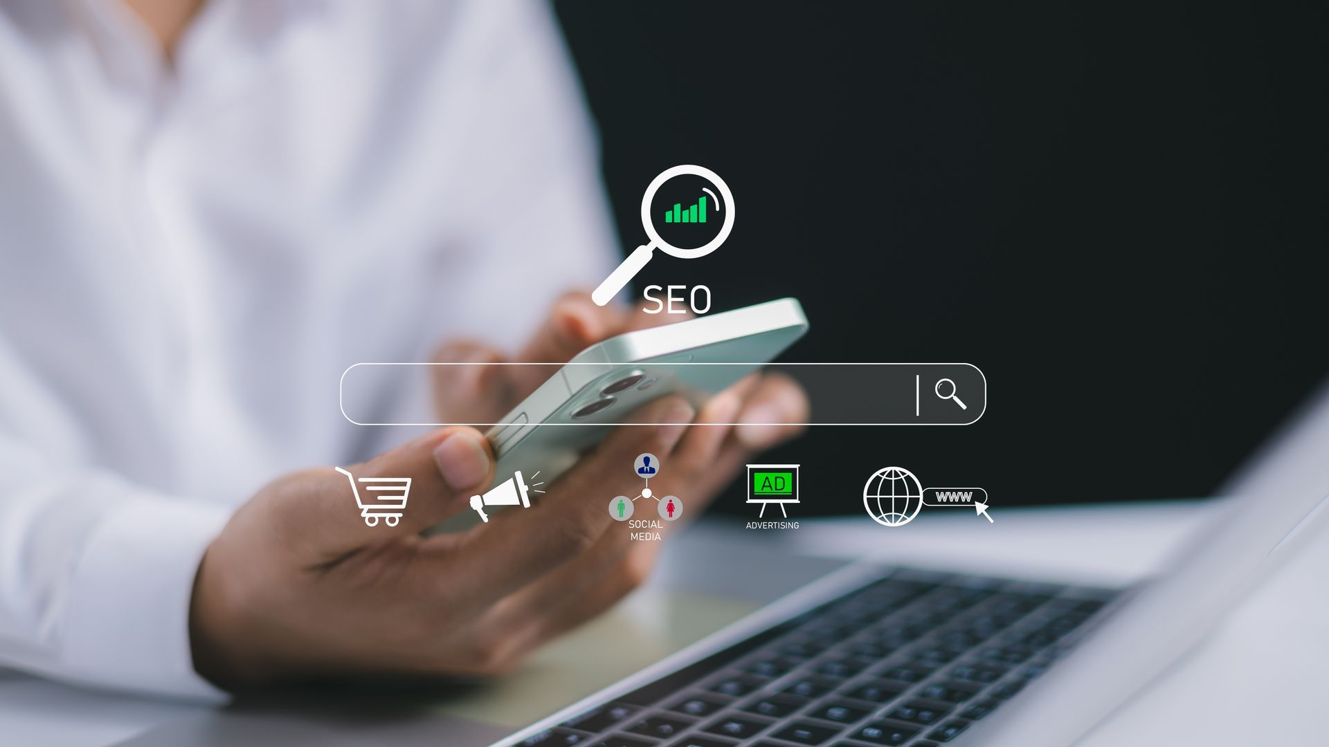 Hand using smartphone over laptop with shopping and search icons, suggesting online shopping