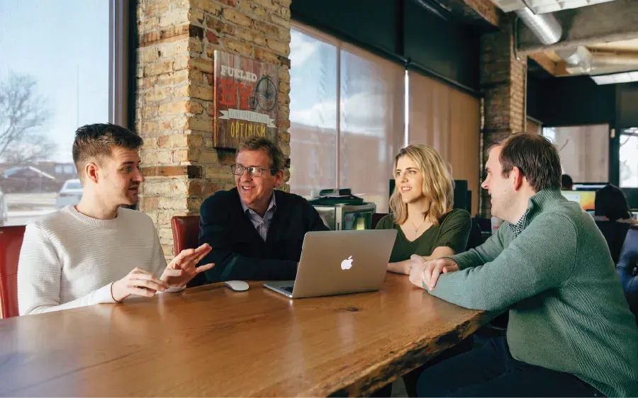 A group of people are sitting around a table with a laptop.
