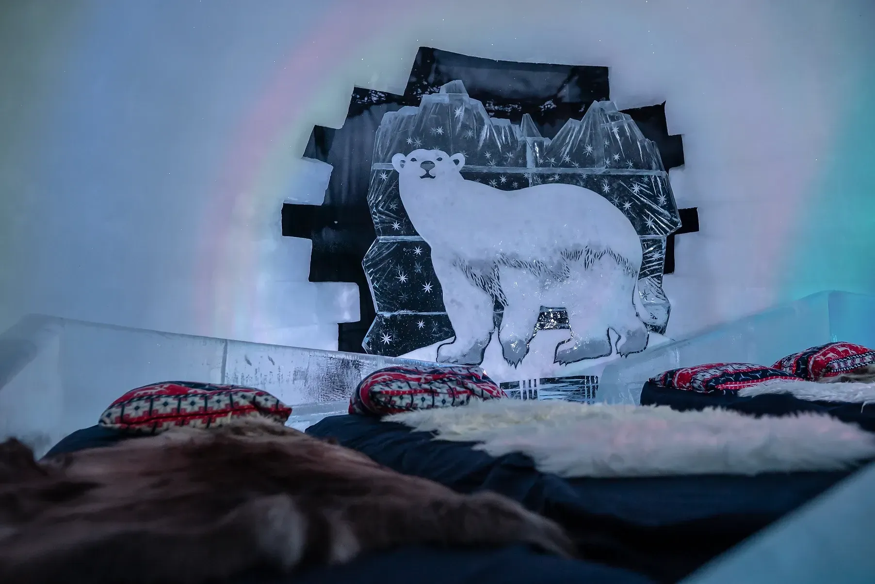 A bed with a polar bear sculpture on the wall behind it inside an igloo in Norway.