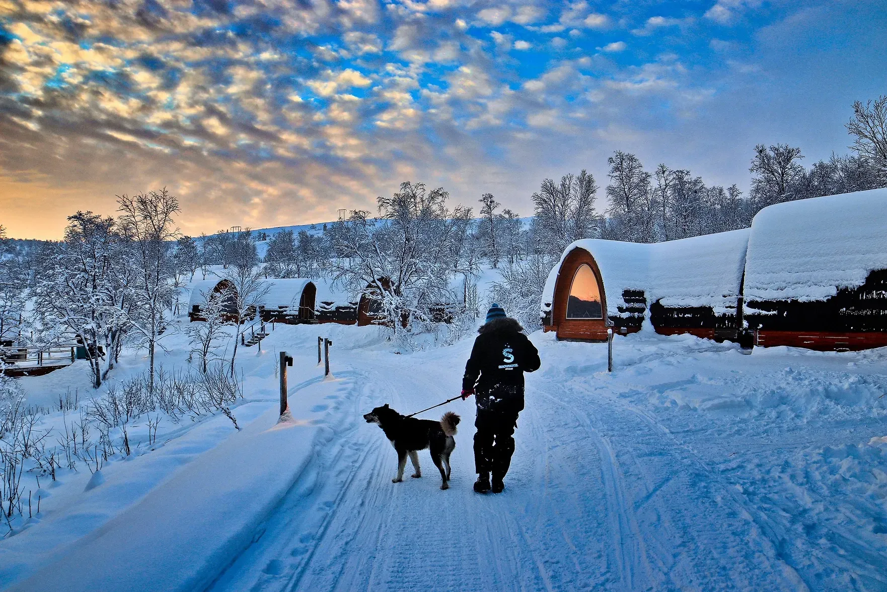 A man is walking a dog on a snowy path in Norway.