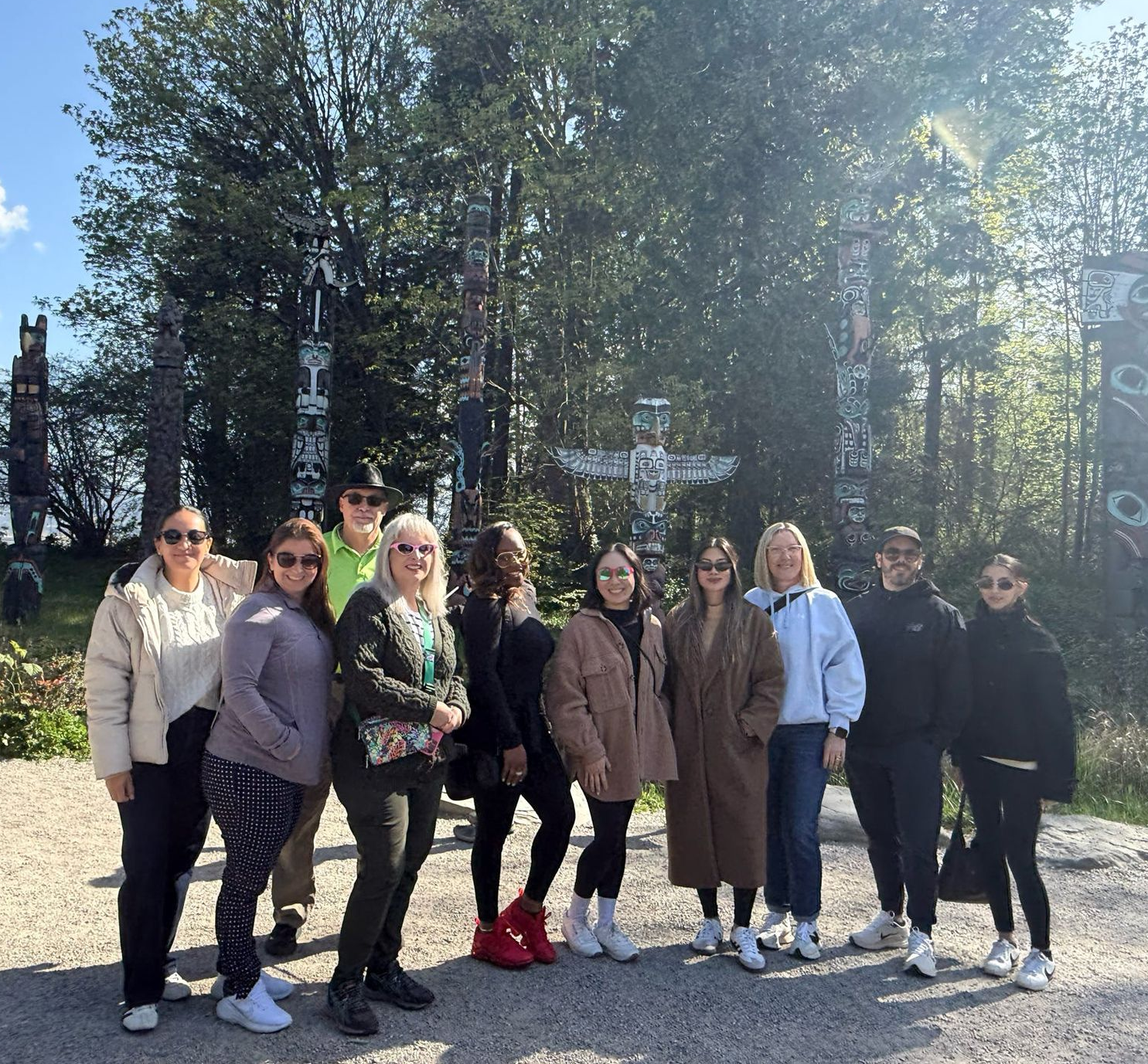 Group of people posing outdoors on a sunny trail with tall trees in the background.