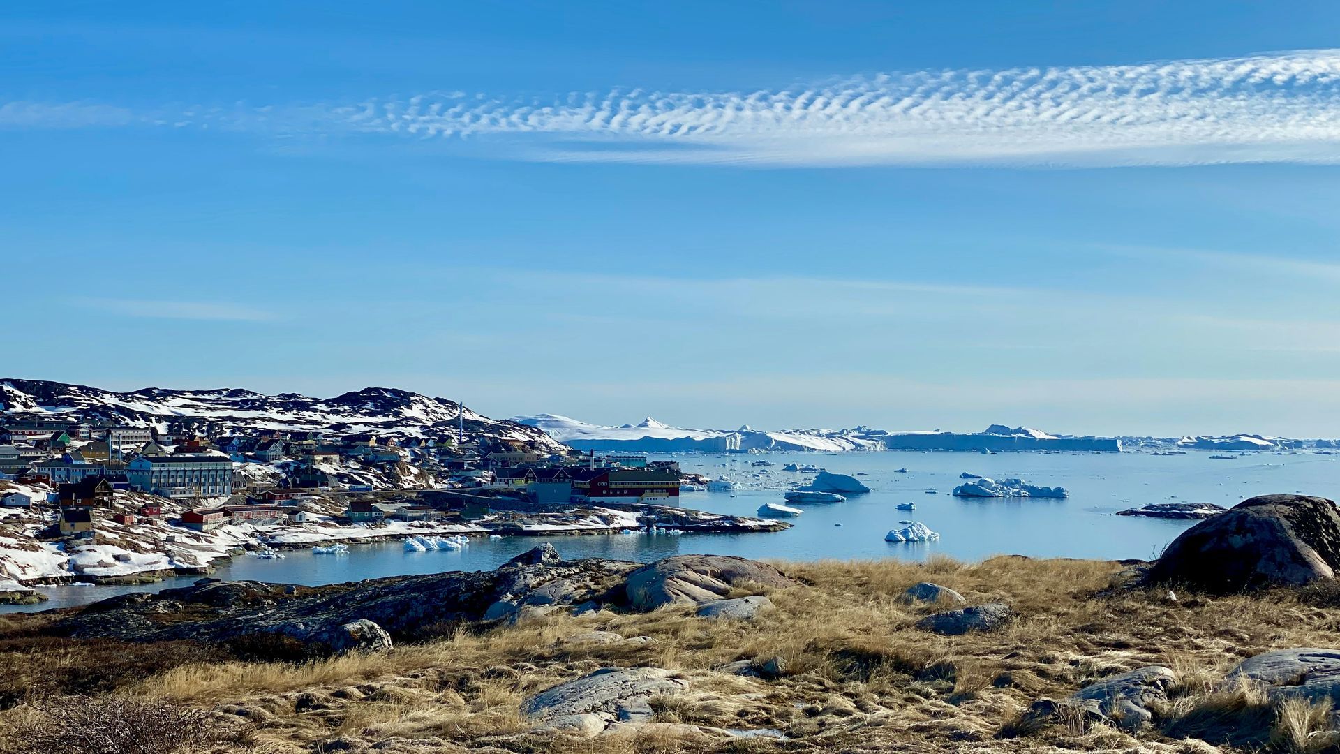 Town of Ilulissat next to icy waters, under a clear blue sky with a few clouds in Greenland.