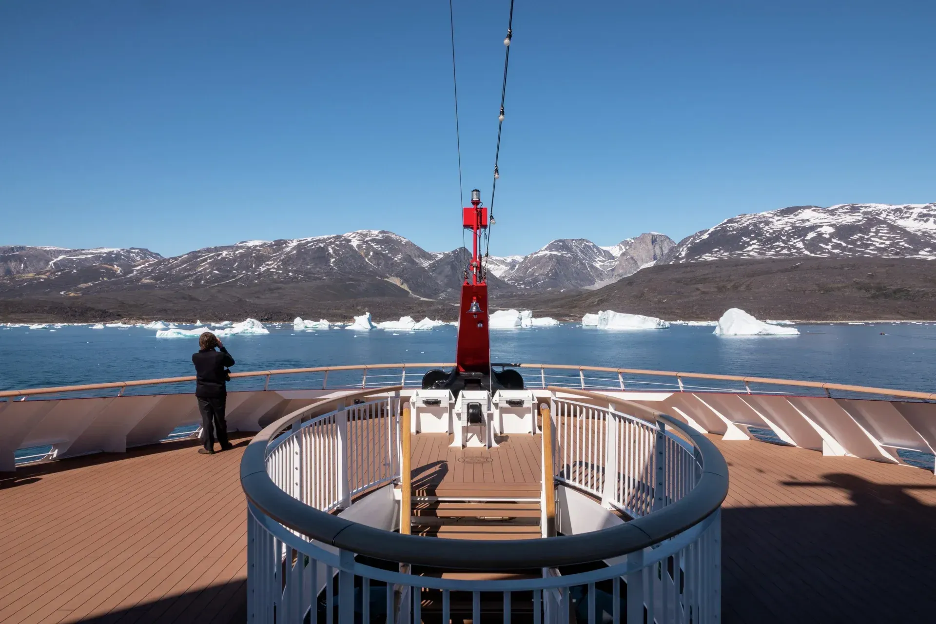 A man is standing on the deck of Hurtigruten Expeditions' MS Fridtjof Nansen cruise ship, looking at icebergs in the water.