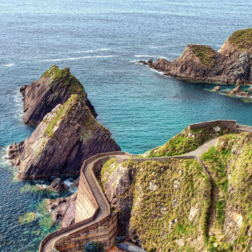 Winding road along cliffs, turquoise water, rocky outcrops, and green vegetation on the Dingle Peninsula, Ireland.